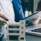 Planujesz jak zacząć zarządzanie nieruchomościami? Model budynku, kalkulator i laptop sugerują analizę inwestycji.