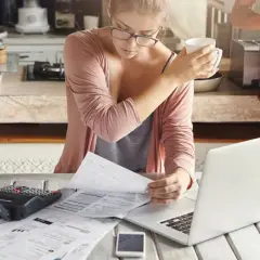 Kobieta z kubkiem w dłoni analizuje dokumenty, by jak obliczyć rentowność najmu. Obok laptop i kalkulator.