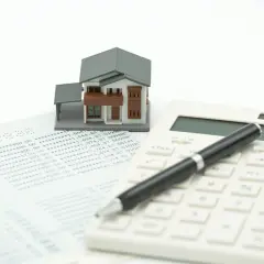 Model domu, kalkulator i dokumenty finansowe sugerują pytanie: kto płaci podatek od nieruchomości właściciel czy najemca?
