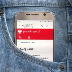 Telefon w kieszeni dżinsów wyświetla stronę podatki.gov.pl, gdzie można sprawdzić, jak zaokrąglić podatek od najmu.