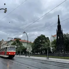 Czerwony tramwaj jedzie ulicą w Pradze. W tle widać pomnik i budynki. Zastanawiasz się, ile kosztuje mieszkanie w Czechach?
