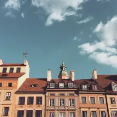 Kamienice z czerwonymi dachami i zieloną wieżą pod błękitnym niebem z chmurami.