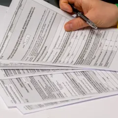 Dłoń z długopisem nad stosem dokumentów PIT, w tym formularzem PIT-28.
