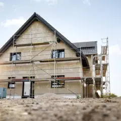 Dom w budowie, rusztowania, piasek. Zastanawiasz się, ile można zarobić na budowie i sprzedaży domu?