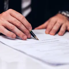 Dłoń z piórem nad dokumentem. Zastanawiasz się, ile trwa wykreślenie hipoteki? Czas zależy od wielu czynników.