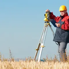 Geodeta w żółtym kasku pracuje z niwelatorem. Zastanawiasz się, ile kosztuje geodeta przy budowie domu?