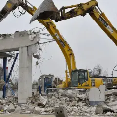 Dwie koparki niszczą betonowy budynek. Zastanawiasz się, ile kosztuje wyburzenie starego domu?