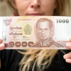 Kobieta trzyma banknot 1000 bahtów, co może pomóc w oszacowaniu, ile kosztuje życie w Tajlandii.