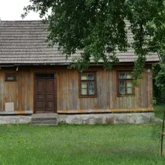 Drewniany dom z gontowym dachem, otoczony zielenią. Widać tu, kiedy dom jest zabytkiem, z jego wiekową, ale wciąż piękną fasadą.