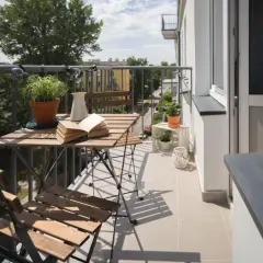 Przytulny balkon z drewnianym stolikiem i krzesłami, roślinami i lampkami. Zastanawiasz się, ile kosztuje balkon przyczepny?