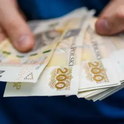 Dłonie trzymają plik banknotów 200 zł. Czy podatek od nieruchomości jest w czynszu?