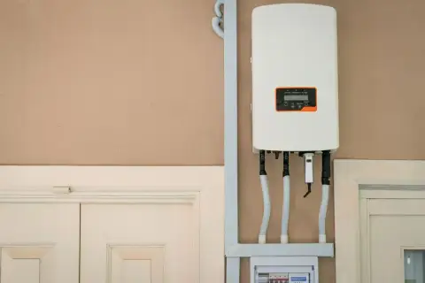 Falownik fotowoltaiczny na ścianie. Urządzenie z wyświetlaczem, podłączone przewodami. Pomaga jak obliczyć kw.