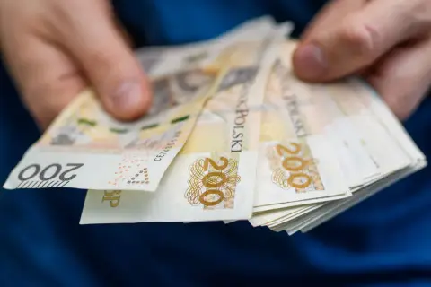 Dłonie trzymają plik banknotów 200 zł. Czy podatek od nieruchomości jest w czynszu?