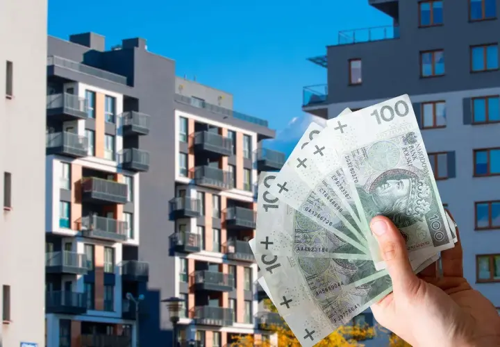 Dłoń trzyma banknoty 100 zł na tle nowoczesnych bloków mieszkalnych. Zastanawiasz się, ile kosztuje wynajem mieszkania w Polsce?
