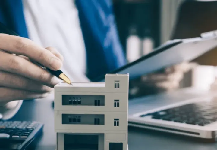 Planujesz jak zacząć zarządzanie nieruchomościami? Model budynku, kalkulator i laptop sugerują analizę inwestycji.