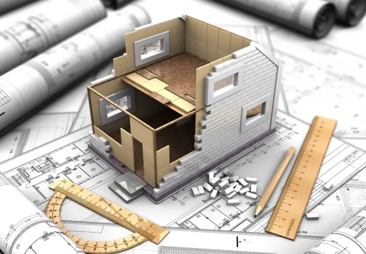 Model domu w budowie na planach architektonicznych, linijka i ołówek. Jak zalegalizować budynek? Zaczynamy od projektu.