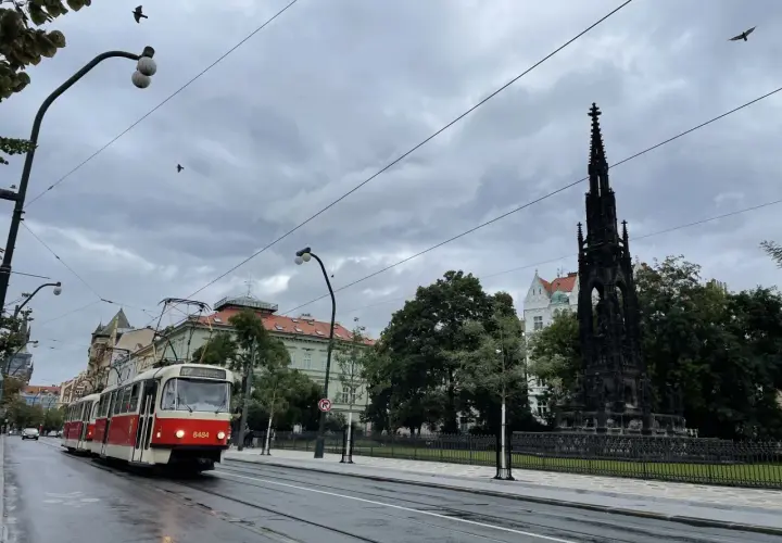 Czerwony tramwaj jedzie ulicą w Pradze. W tle widać pomnik i budynki. Zastanawiasz się, ile kosztuje mieszkanie w Czechach?