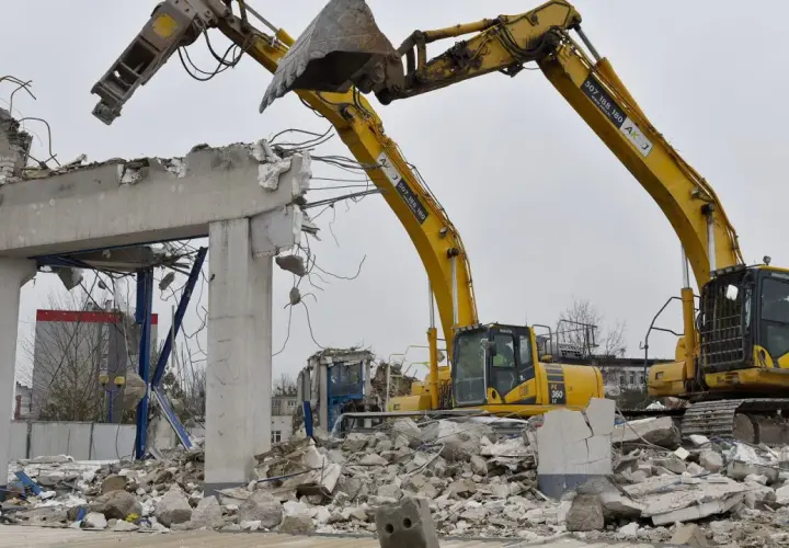 Dwie koparki niszczą betonowy budynek. Zastanawiasz się, ile kosztuje wyburzenie starego domu?