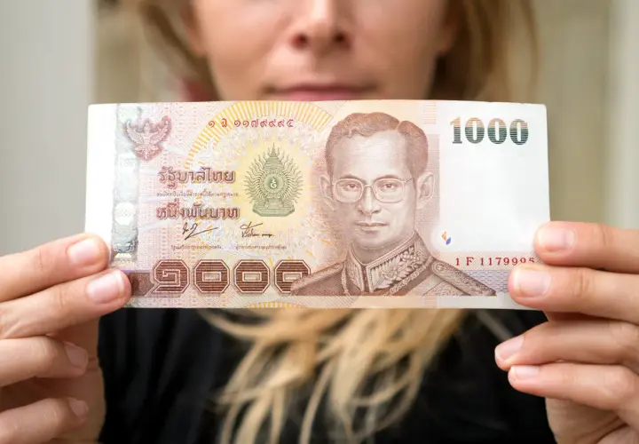 Kobieta trzyma banknot 1000 bahtów, co może pomóc w oszacowaniu, ile kosztuje życie w Tajlandii.