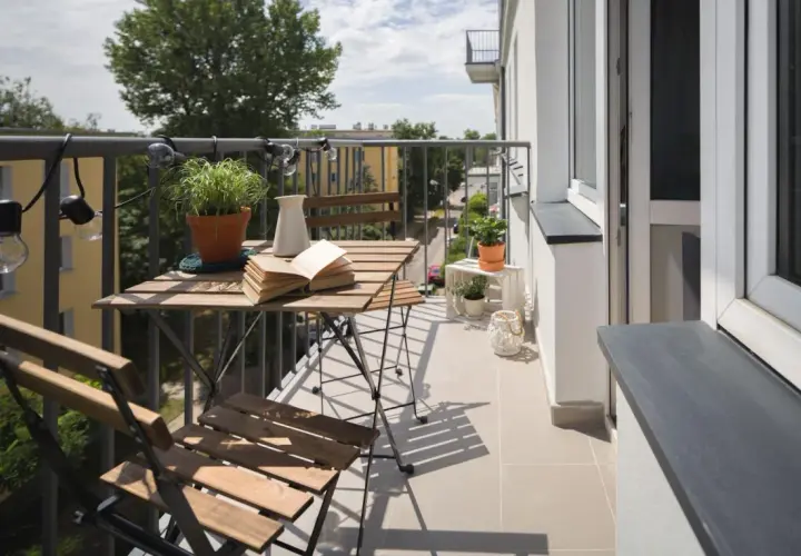 Przytulny balkon z drewnianym stolikiem i krzesłami, roślinami i lampkami. Zastanawiasz się, ile kosztuje balkon przyczepny?