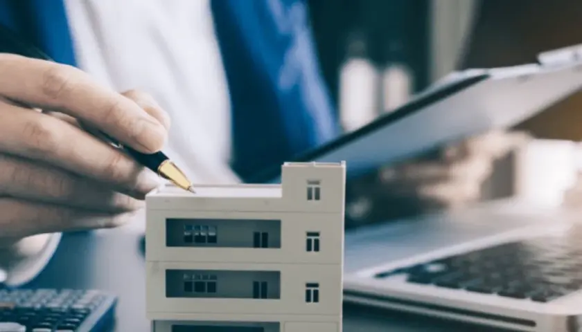 Planujesz jak zacząć zarządzanie nieruchomościami? Model budynku, kalkulator i laptop sugerują analizę inwestycji.