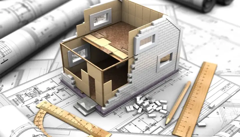 Model domu w budowie na planach architektonicznych, linijka i ołówek. Jak zalegalizować budynek? Zaczynamy od projektu.