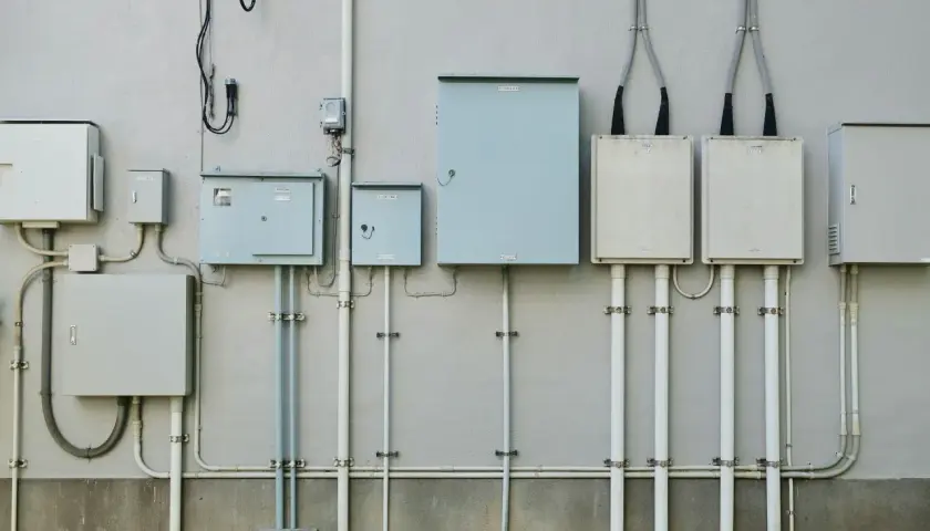 Szereg skrzynek elektrycznych i rur na ścianie budynku, przygotowanie do podłączenia prądu do działki bez domu.