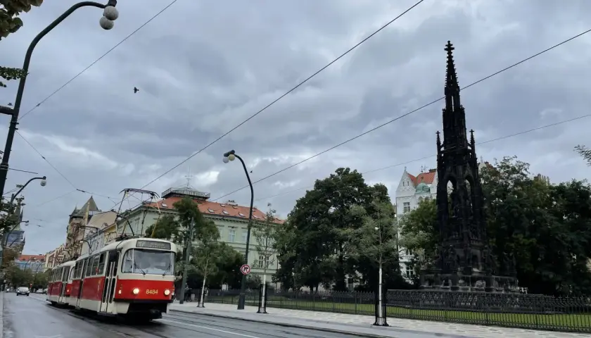 Czerwony tramwaj jedzie ulicą w Pradze. W tle widać pomnik i budynki. Zastanawiasz się, ile kosztuje mieszkanie w Czechach?