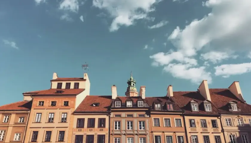 Kamienice z czerwonymi dachami i zieloną wieżą pod błękitnym niebem z chmurami.