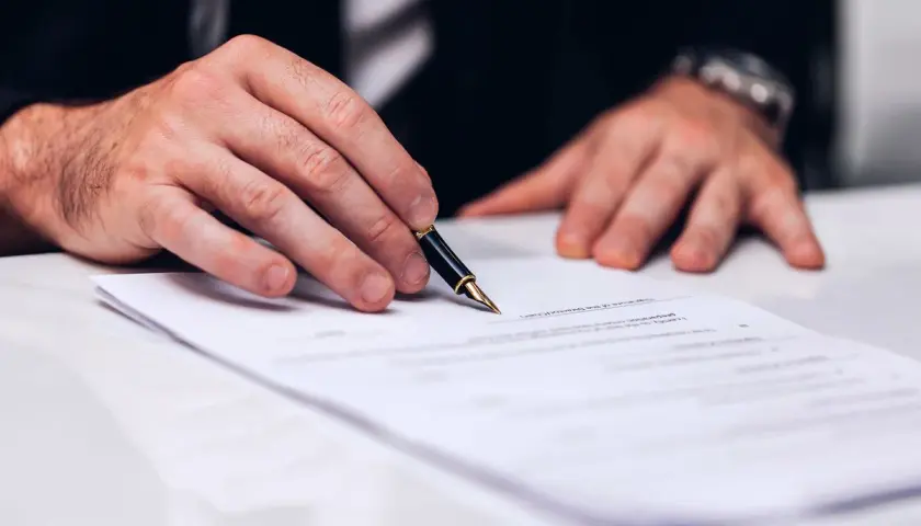 Dłoń z piórem nad dokumentem. Zastanawiasz się, ile trwa wykreślenie hipoteki? Czas zależy od wielu czynników.