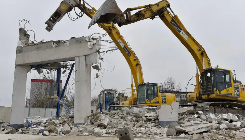 Dwie koparki niszczą betonowy budynek. Zastanawiasz się, ile kosztuje wyburzenie starego domu?