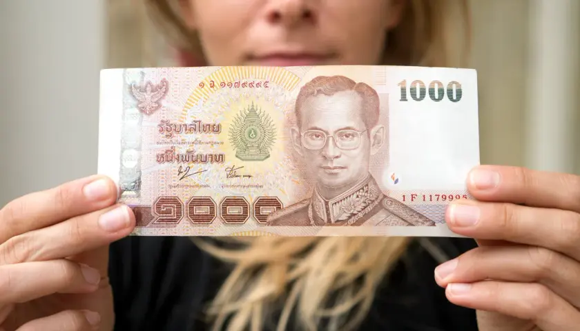 Kobieta trzyma banknot 1000 bahtów, co może pomóc w oszacowaniu, ile kosztuje życie w Tajlandii.