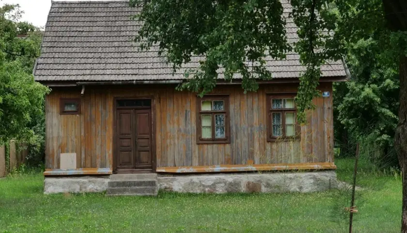 Drewniany dom z gontowym dachem, otoczony zielenią. Widać tu, kiedy dom jest zabytkiem, z jego wiekową, ale wciąż piękną fasadą.