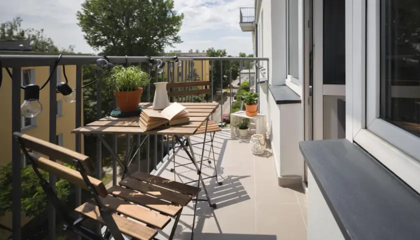 Przytulny balkon z drewnianym stolikiem i krzesłami, roślinami i lampkami. Zastanawiasz się, ile kosztuje balkon przyczepny?