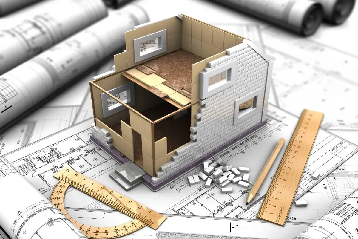 Model domu w budowie na planach architektonicznych, linijka i ołówek. Jak zalegalizować budynek? Zaczynamy od projektu.