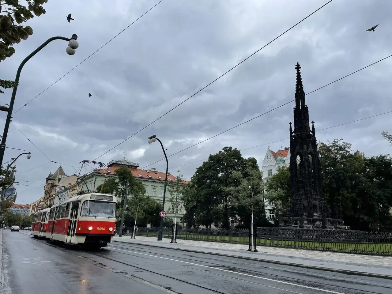 Czerwony tramwaj jedzie ulicą w Pradze. W tle widać pomnik i budynki. Zastanawiasz się, ile kosztuje mieszkanie w Czechach?