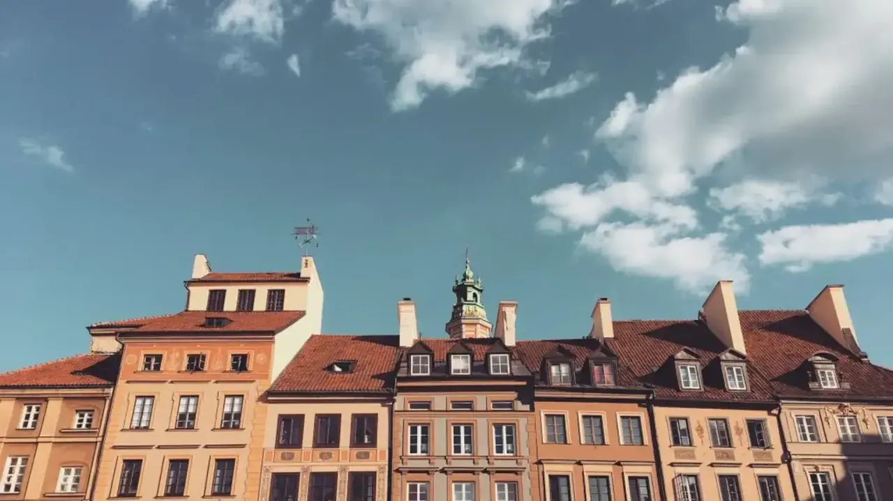 Kamienice z czerwonymi dachami i zieloną wieżą pod błękitnym niebem z chmurami.
