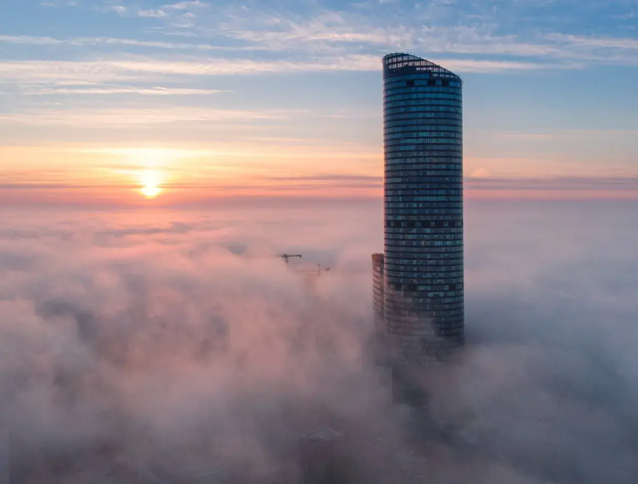 Wrocławski Sky Tower wyłaniający się z mgły o wschodzie słońca.
