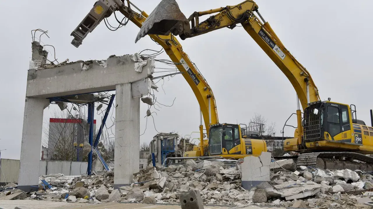 Dwie koparki niszczą betonowy budynek. Zastanawiasz się, ile kosztuje wyburzenie starego domu?