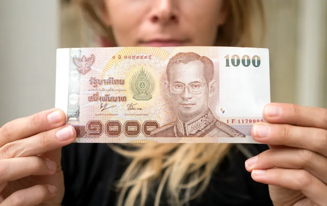 Kobieta trzyma banknot 1000 bahtów, co może pomóc w oszacowaniu, ile kosztuje życie w Tajlandii.