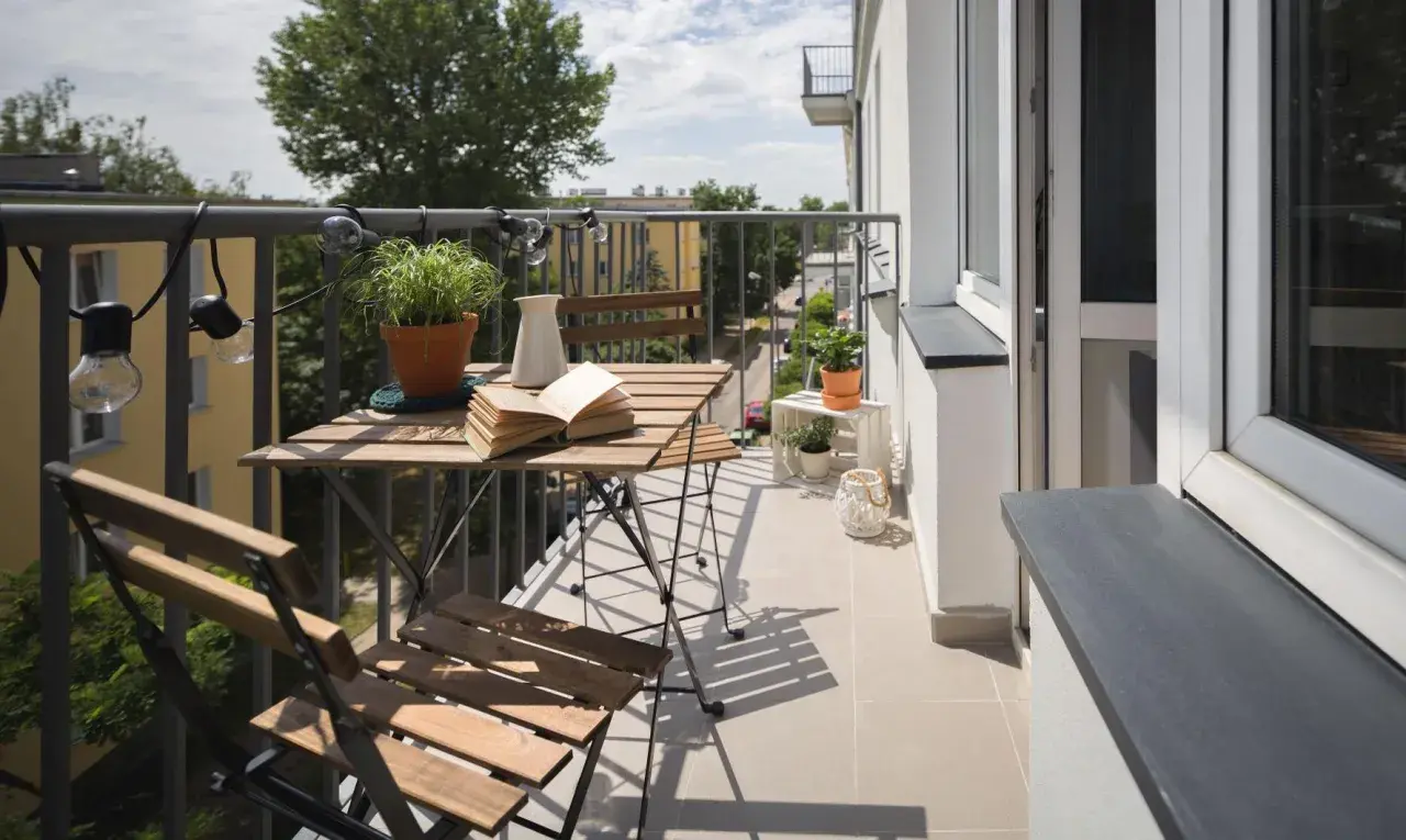 Przytulny balkon z drewnianym stolikiem i krzesłami, roślinami i lampkami. Zastanawiasz się, ile kosztuje balkon przyczepny?
