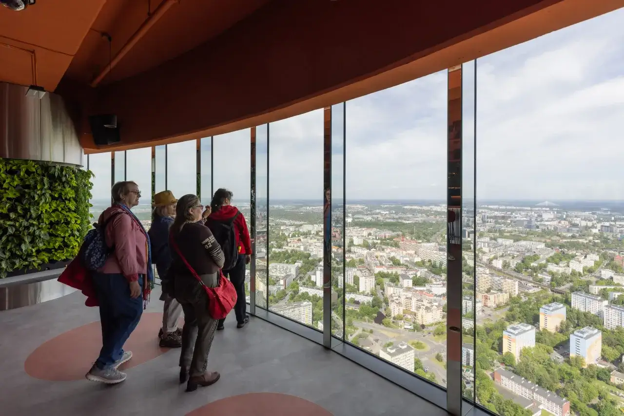 Grupa osób podziwia panoramę miasta z tarasu widokowego. Zastanawiają się, ile Sky Tower ma pięter, patrząc na rozległy krajobraz z wysokości.