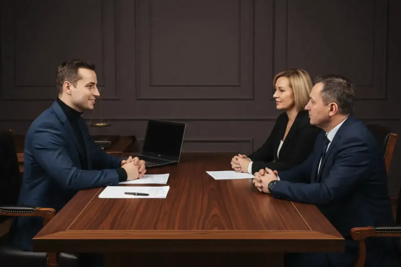 Trzy osoby przy stole omawiają umowę. Prawnik wyjaśnia, kto płaci za notariusza przy sprzedaży domu.