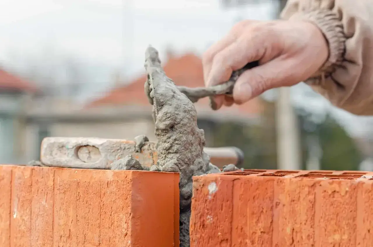 Budowa domu z budynku gospodarczego może grozić karą. Murarz kładzie cegły, przygotowując fundamenty.