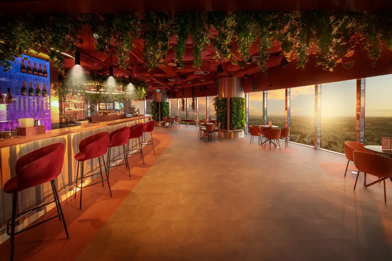 Elegancki bar z widokiem na miasto o zachodzie słońca. Wnętrze ozdobione zielenią, z czerwonymi krzesłami i stołami. Ile Sky Tower ma pięter? To pytanie pozostaje bez odpowiedzi, ale widok z tego miejsca jest zachwycający.
