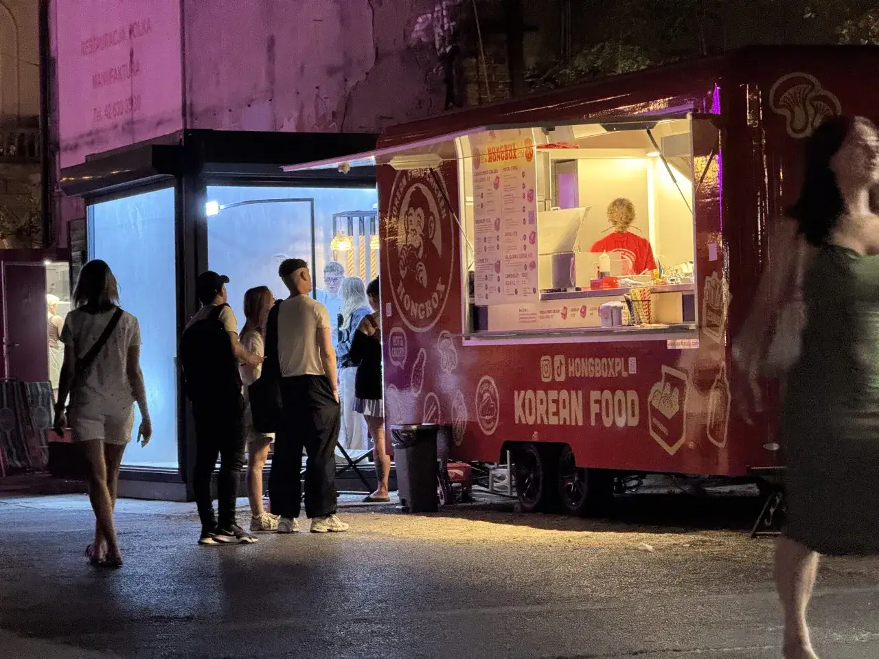 Ludzie stoją w kolejce do czerwonego food trucka z koreańskim jedzeniem. Widać menu i pracownika. To świetny sposób, by dowiedzieć się, jak zamówić food trucka.
