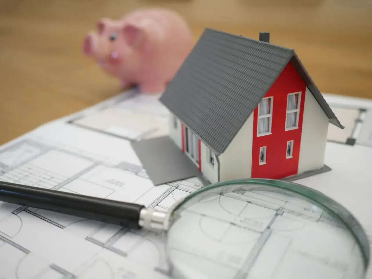 Model domu, szkło powiększające i świnka skarbonka na planach architektonicznych. Zastanawiasz się, co to jest odstępne za mieszkanie?