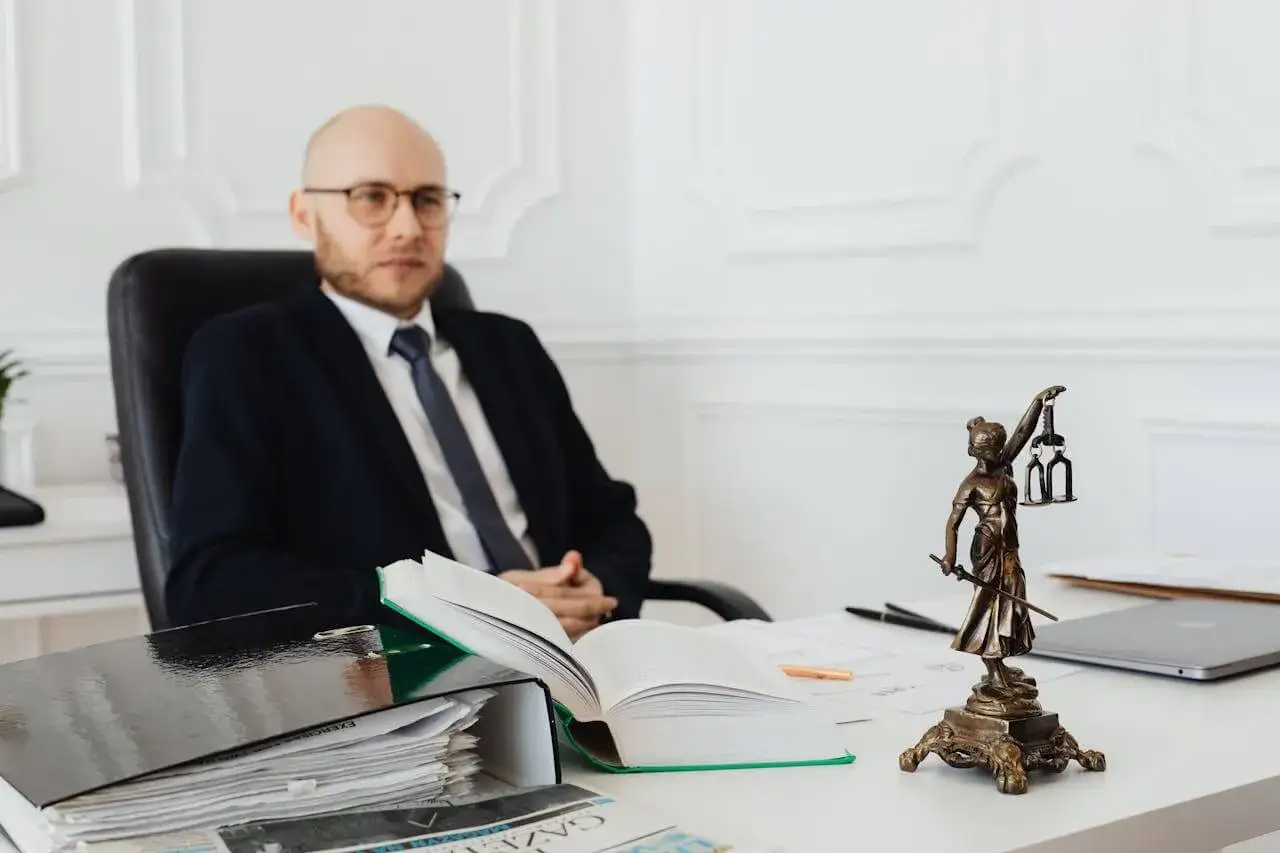 Prawnik w garniturze siedzi przy biurku z dokumentami. Na biurku figurka Temidy i otwarta księga. Kto płaci za notariusza przy sprzedaży domu?