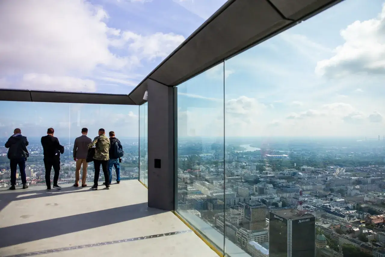 Pięciu mężczyzn podziwia panoramę Warszawy z tarasu widokowego. Z tej wysokości trudno ocenić, ile pięter ma warsaw tower, ale widok jest imponujący.
