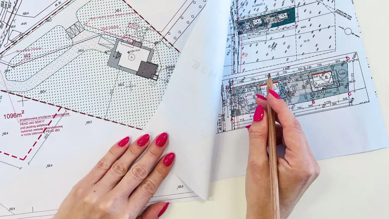 Kobieta z różowymi paznokciami analizuje mapę geodezyjną. Zastanawia się, ile kosztuje geodeta przy budowie domu, porównując dane na dokumentach.